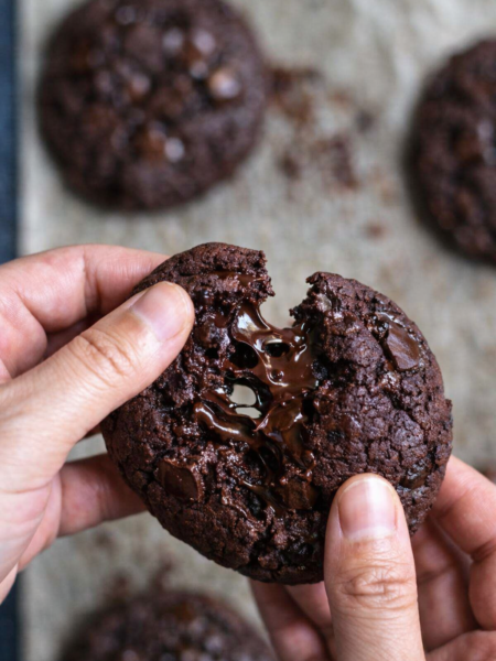 Cookie double chocolat cassé en deux, cœur fondant et morceaux de chocolat noir fondus, photo culinaire rustique sur fond en bois.