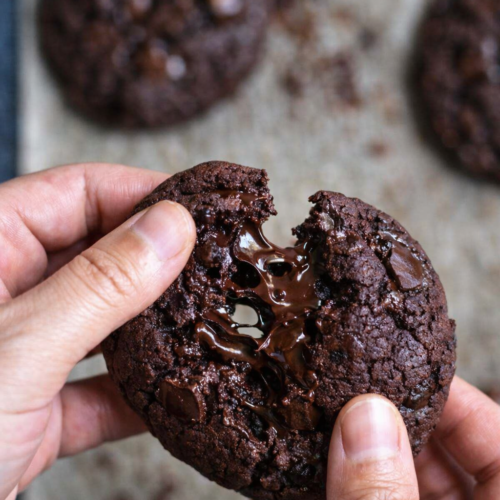 Cookie double chocolat cassé en deux, cœur fondant et morceaux de chocolat noir fondus, photo culinaire rustique sur fond en bois.