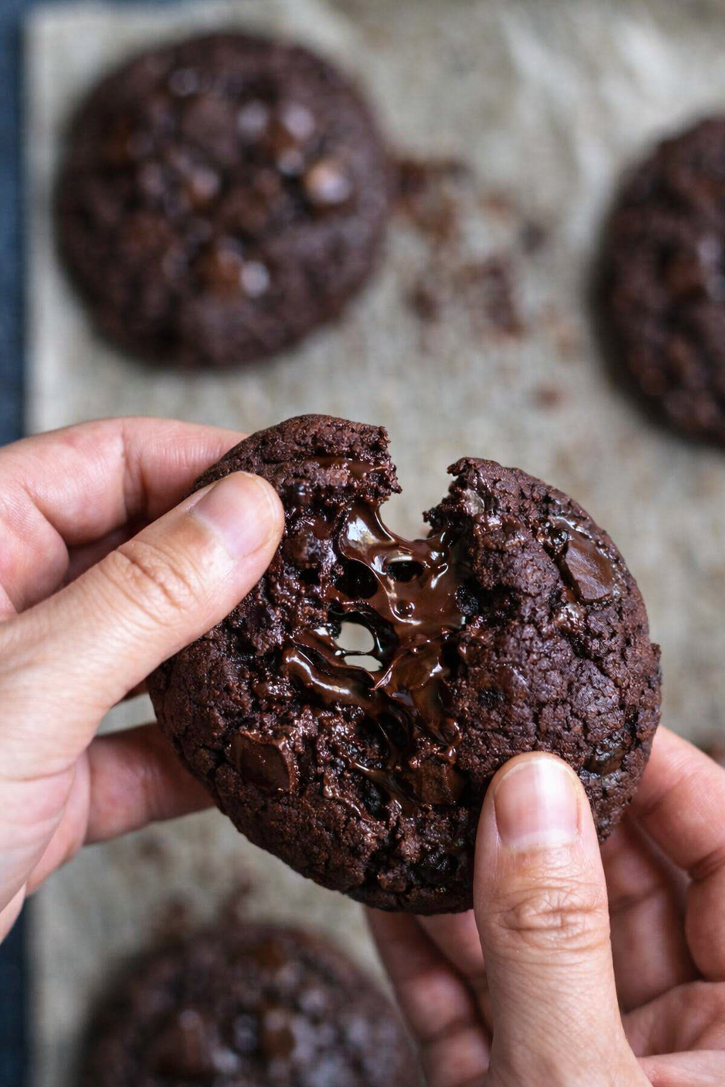 Cookie double chocolat cassé en deux, cœur fondant et morceaux de chocolat noir fondus, photo culinaire rustique sur fond en bois.