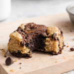 Brookie maison partiellement croqué, mélange fondant de pâte à brownie et pâte à cookie, posé sur une planche en bois clair avec quelques pépites de chocolat autour.