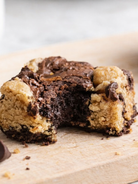 Brookie maison partiellement croqué, mélange fondant de pâte à brownie et pâte à cookie, posé sur une planche en bois clair avec quelques pépites de chocolat autour.