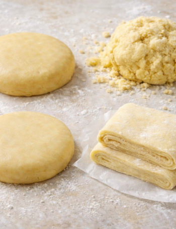 Quatre pâtes de base en pâtisserie — sucrée, sablée, brisée et feuilletée — disposées sur un plan légèrement fariné.