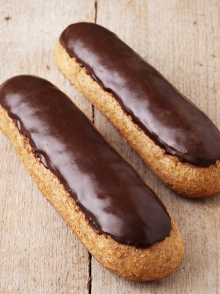 Deux éclairs au chocolat posés sur une table en bois clair rustique, glaçage légèrement mat et pâte à choux dorée.