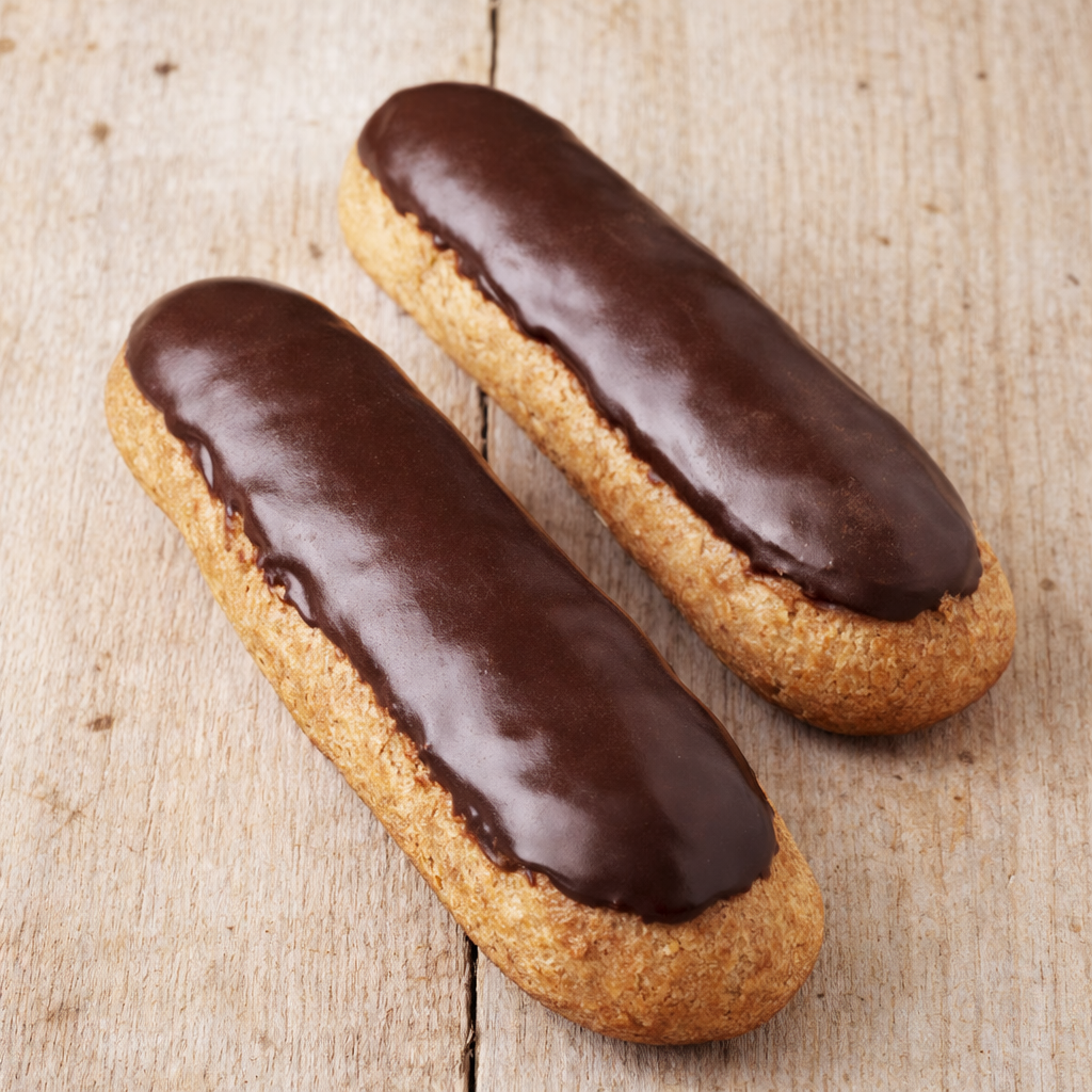 Deux éclairs au chocolat posés sur une table en bois clair rustique, glaçage légèrement mat et pâte à choux dorée.