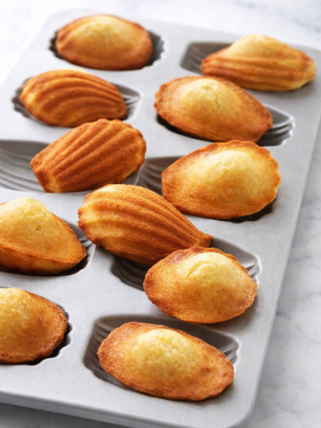 Madeleines maison dorées dans un moule gris clair, éclairées par une lumière naturelle, ambiance gourmande et artisanale.