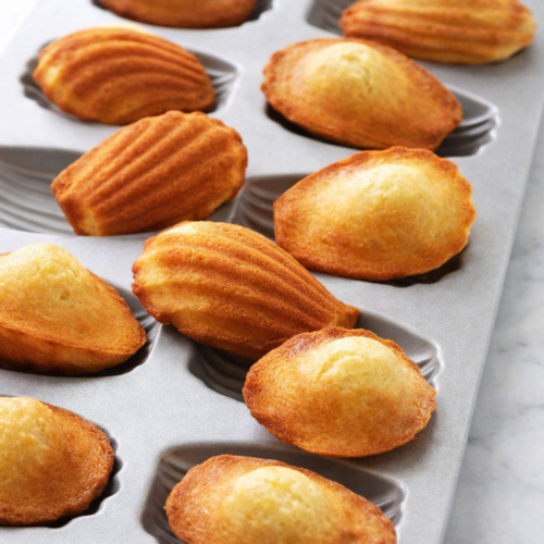 Madeleines maison dorées dans un moule gris clair, éclairées par une lumière naturelle, ambiance gourmande et artisanale.