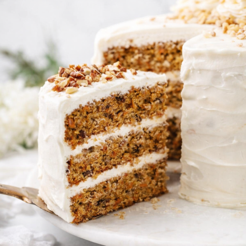 Tranche de carrot cake moelleux aux noix de pécan sur fond lumineux naturel, style éditorial moderne.
