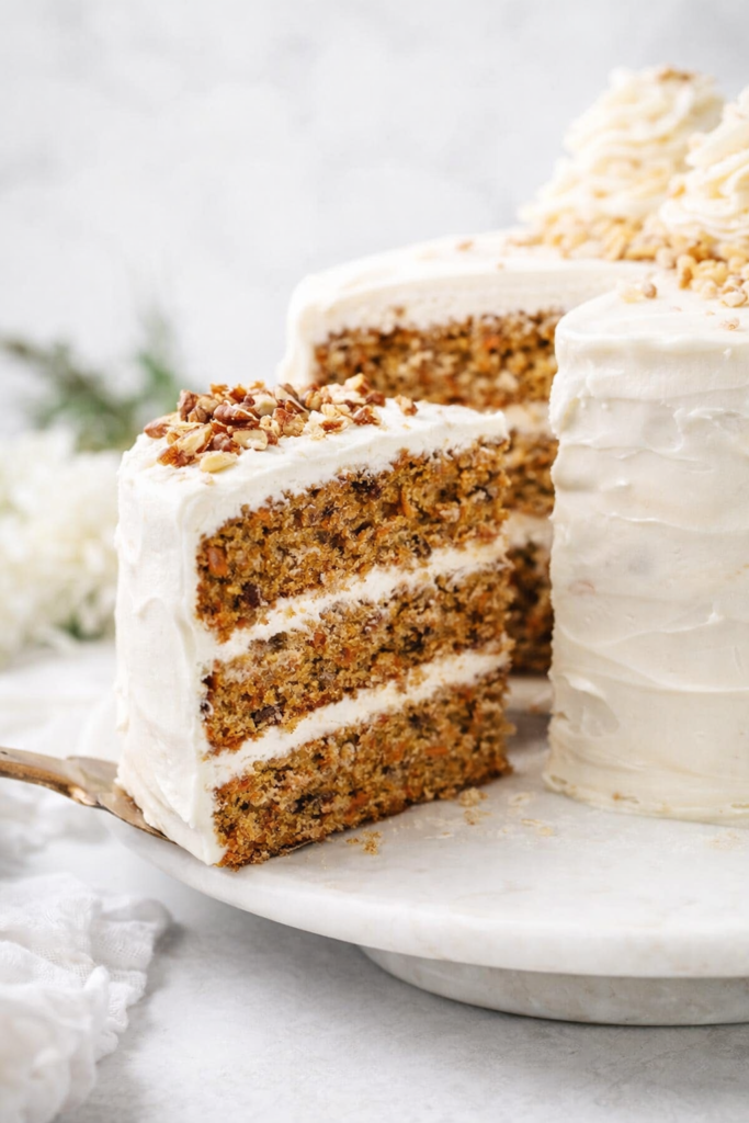 Tranche de carrot cake moelleux aux noix de pécan sur fond lumineux naturel, style éditorial moderne.