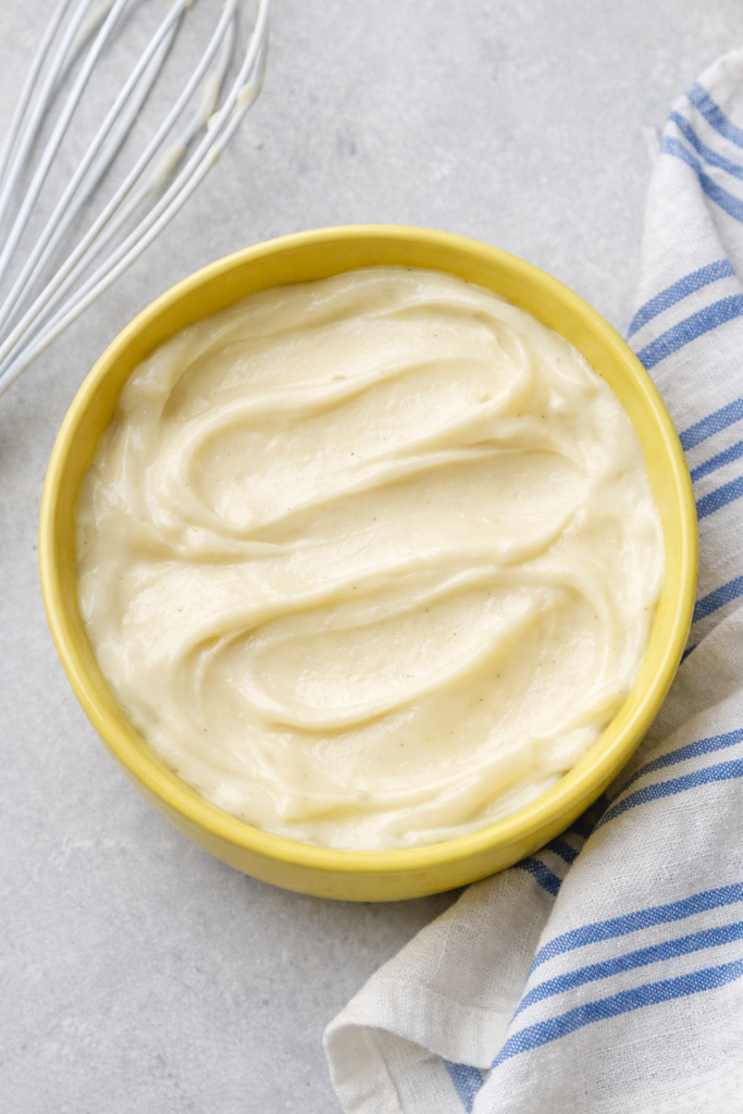 Bol jaune rempli de crème Princesse onctueuse, avec traces de cuillère subtiles, posé sur une serviette blanche et bleue dans une lumière naturelle.