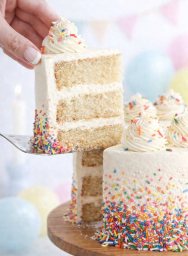 Gâteau vanille à trois étages recouvert d’un dégradé de sprinkles colorés, avec une part soulevée sur une pelle à gâteau.