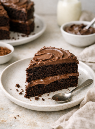 Part de gâteau chocolat vegan servie dans une assiette en céramique, éclairée par la lumière naturelle, avec un décor minimaliste et quelques miettes visibles.