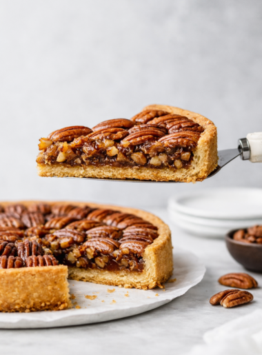 Part de tarte aux noix de pécan soulevée sur une pelle à tarte, montrant la garniture caramélisée et la croûte dorée en lumière naturelle.