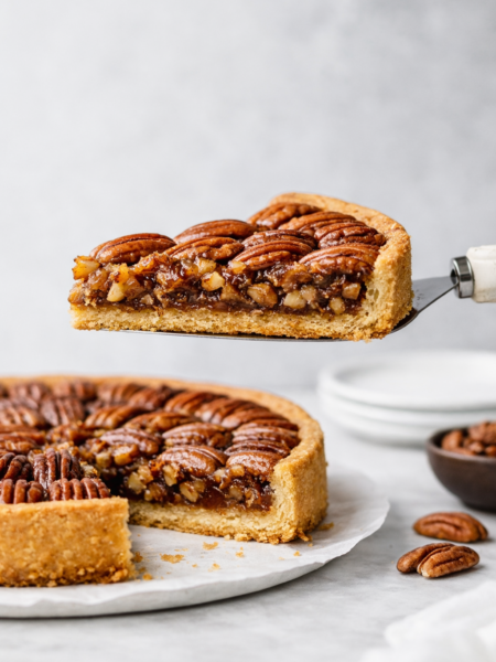 Part de tarte aux noix de pécan soulevée sur une pelle à tarte, montrant la garniture caramélisée et la croûte dorée en lumière naturelle.